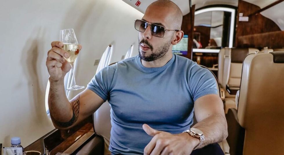 Andrew Tate holding a glass of wine on a plane.