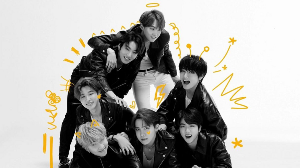 Group photo of BTS with decorative doodles around all seven of them. They are all wearing leather jackets and sporting happy expressions.