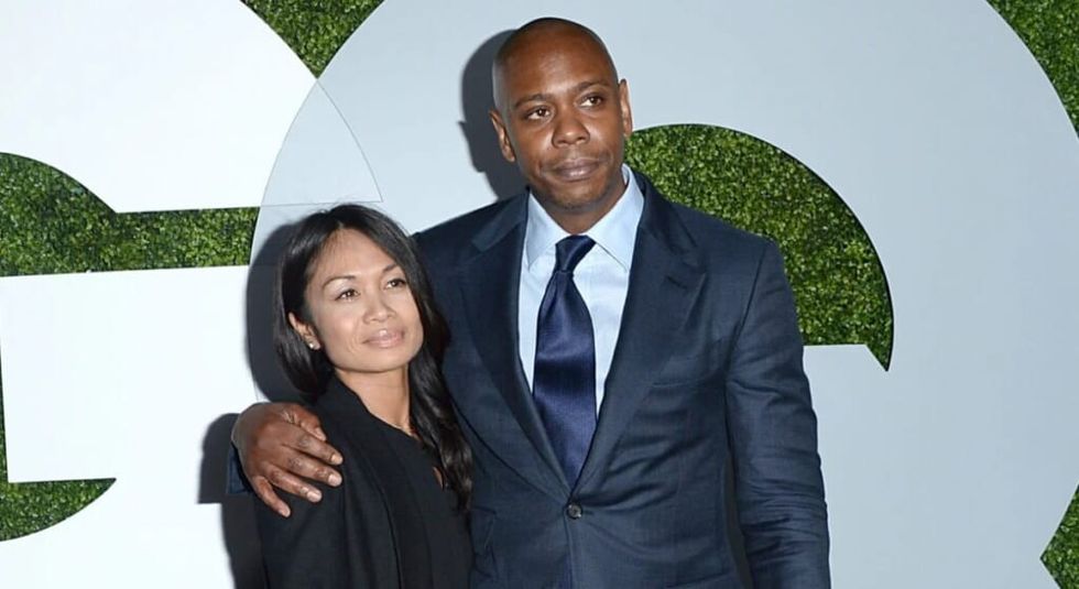 Dave Chappelle in blue suit and tie with wife Elaine wearing black jacket.
