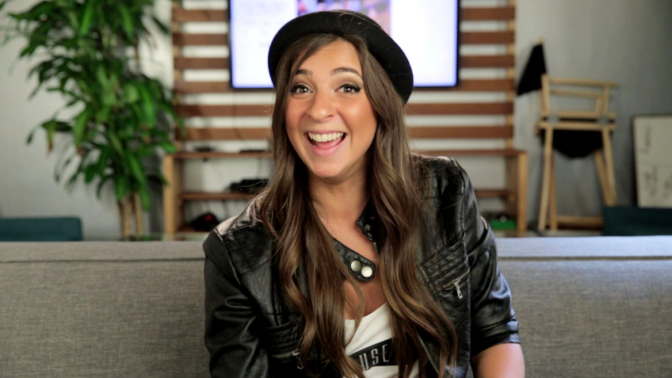 Gabbie Hanna in a black hat and leather jacket, smiling at the camera.