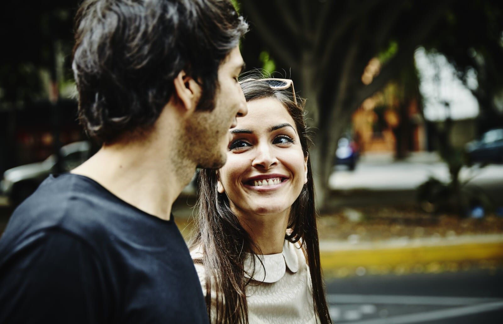 Smiling woman in discussion with boyfriend walking on sidewalk of city street on summer evening