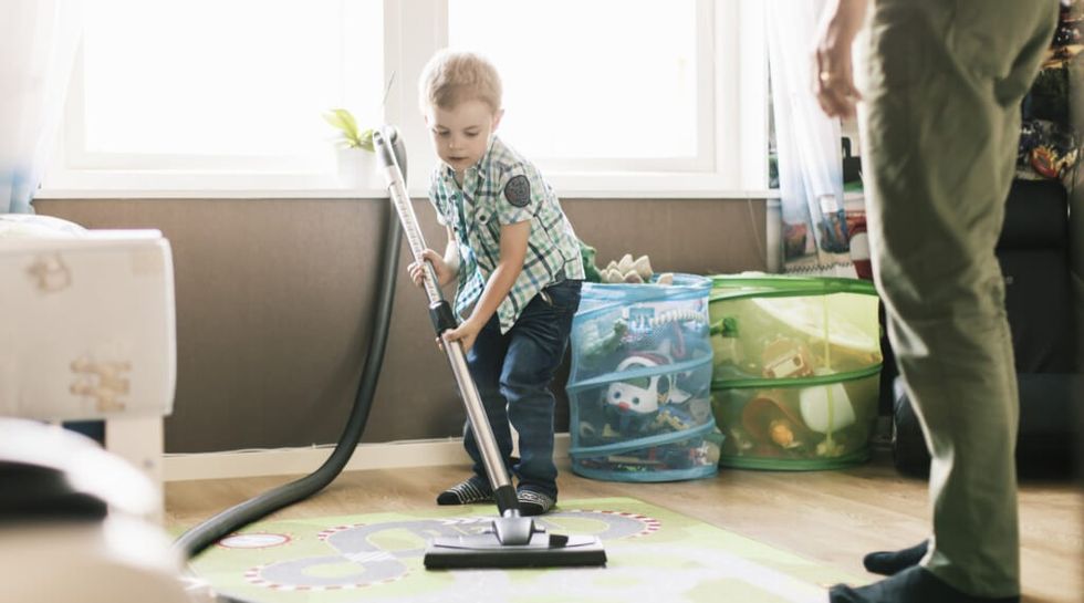 Boy vacuuming floor while father standing at home