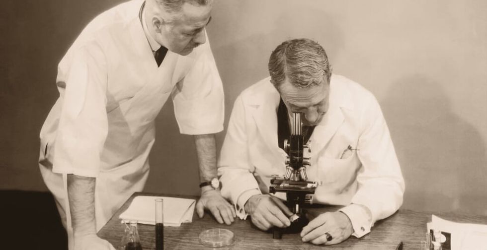 Two men working in laboratory, one looking into microscope