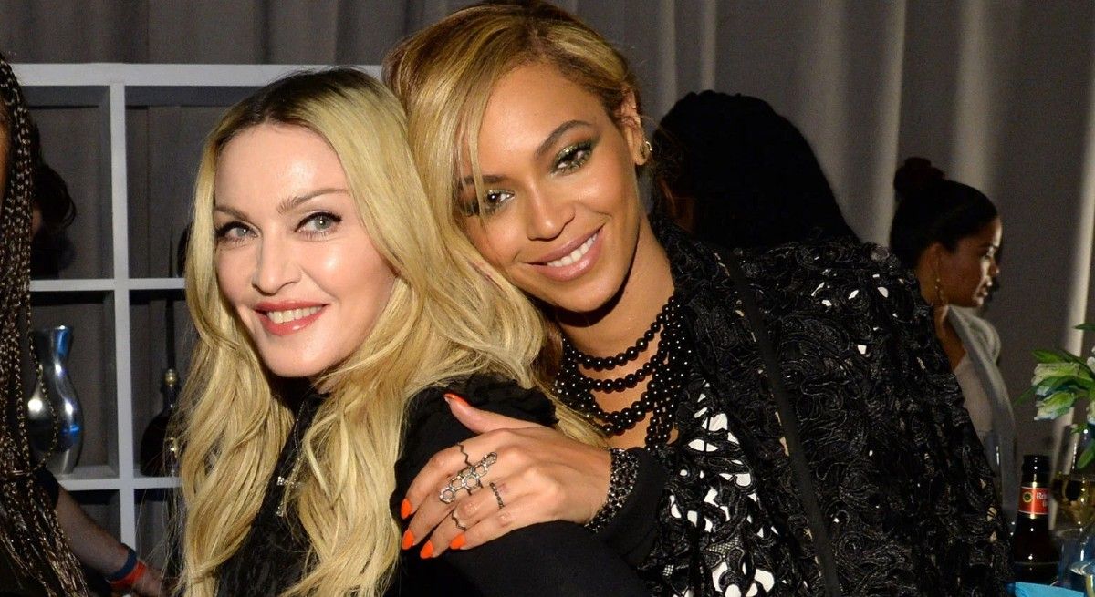 Madonna smiles at the camera while Beyoncé hugs her from behind.