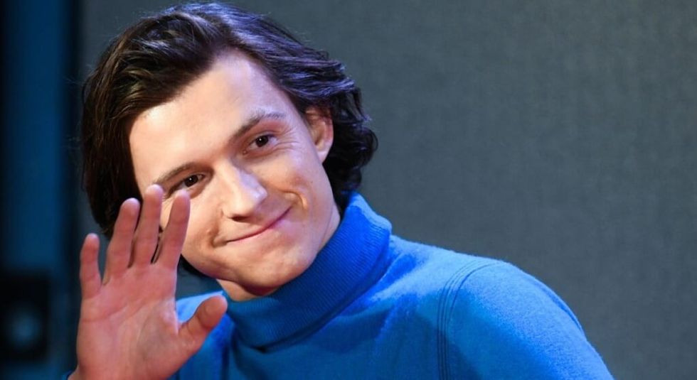 Tom Holland of Superman wearing a blue sweater and waving to the audience.