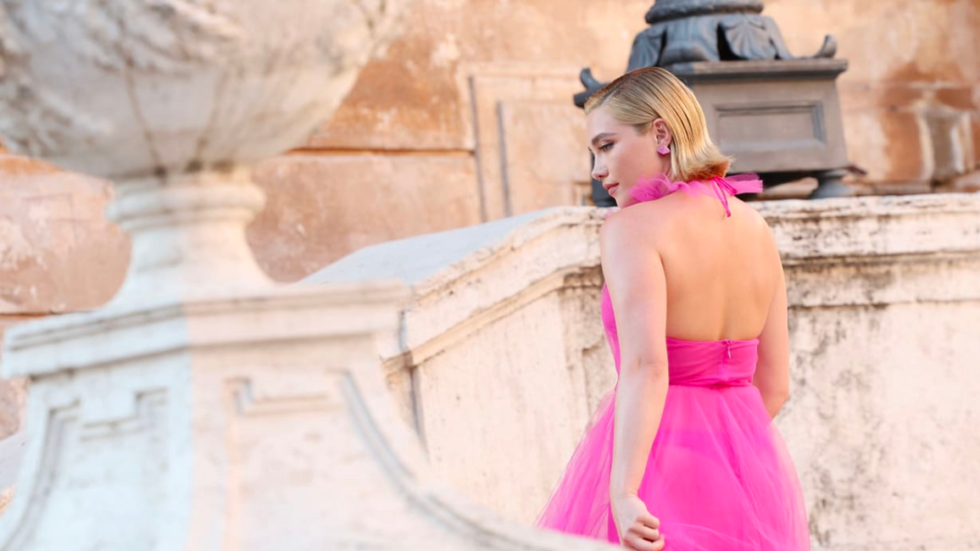 Florence Pugh wearing a hot pink dress, walking up some steps.