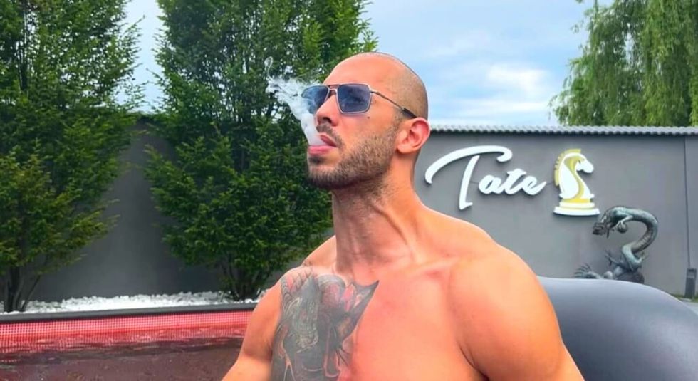 Andrew Tate smoking while showing off chest tattoo.