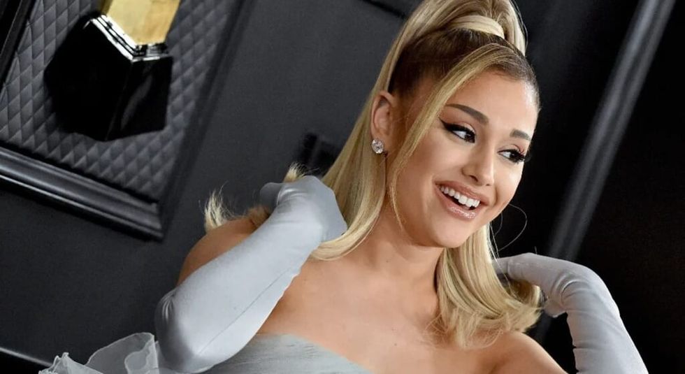 Ariana Grande laughing while wearing blue ball gown and gloves.