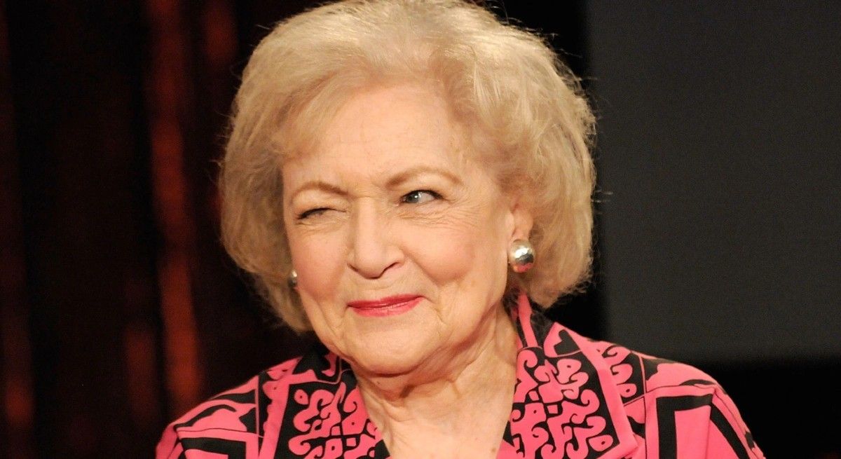 Betty White wearing a pink blouse and winking at the camera.