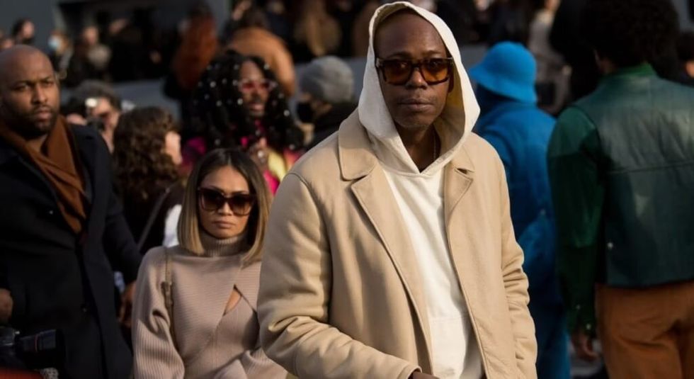 Dave Chappelle in white hoodie at basketball game with wife Elaine.