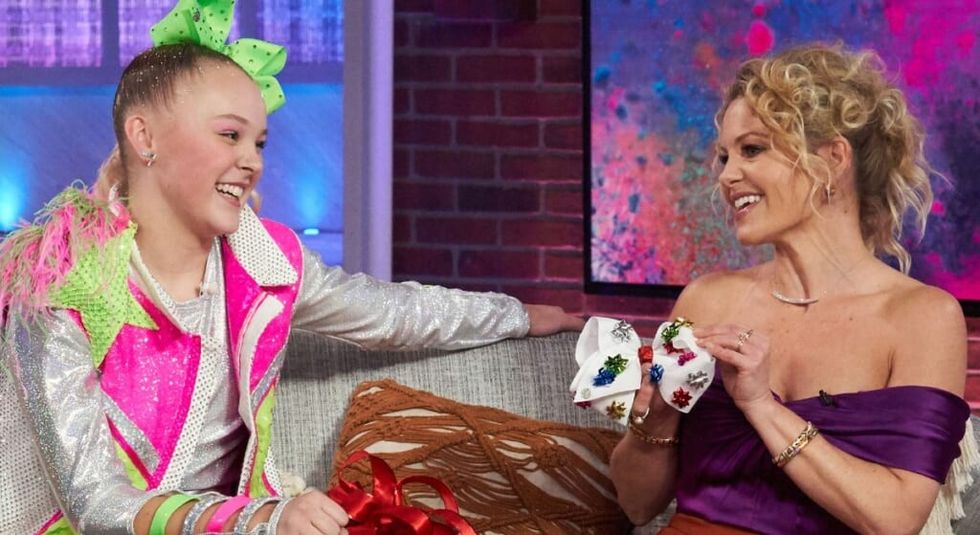JoJo Siwa and Candace Cameron Bure laughing on a couch during an interview.