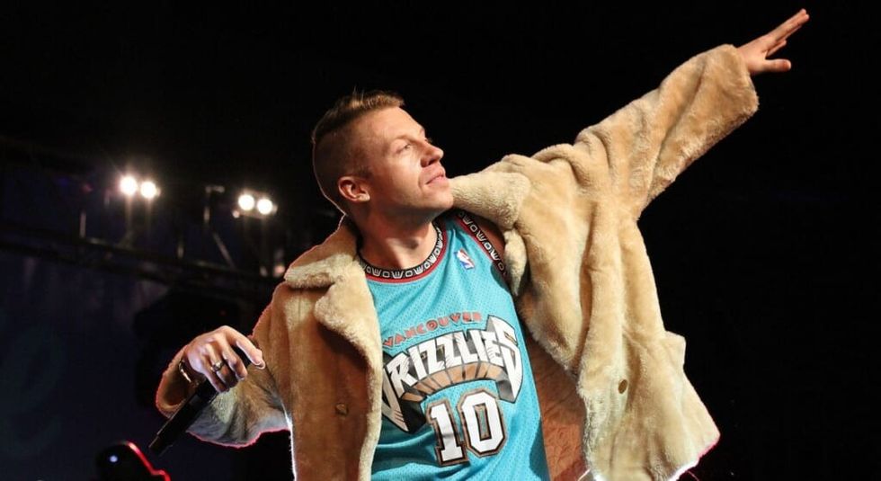 Singer Macklemore performing with arm reached to the sky.