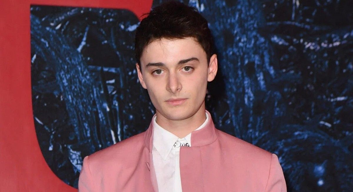 Noah Schnapp on the red carpet wearing a pink jacket and looking serious.