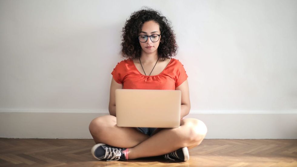woman with glasses sitting on the floor with a laptop on her legs