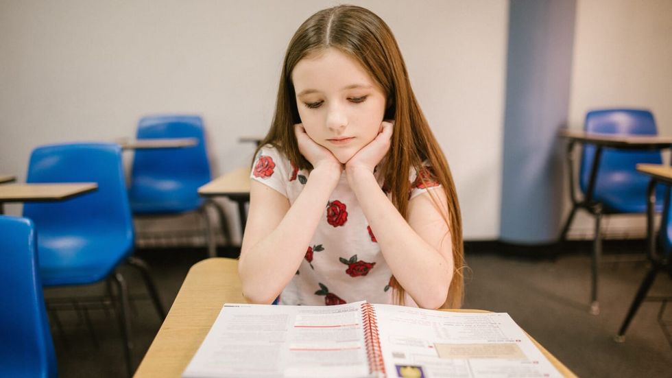 young girl looking sad at a textbook in a classroom