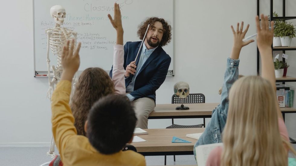 man teaching next to a skeleton in class, children raising their hands