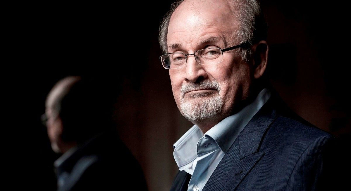 Headshot of Salman Rushdie looking at the camera in blue suit.