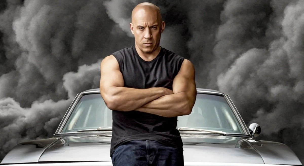 Vin Diesel in The Fast and The Furious with arms crossed sitting on his car.