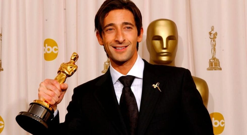 Adrien Brody in black suit and white shirt holding his Oscar statue.