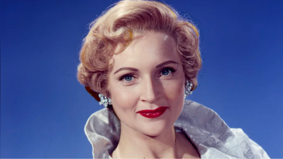 An archival image of a young Betty White wearing earrings and red lipstick.