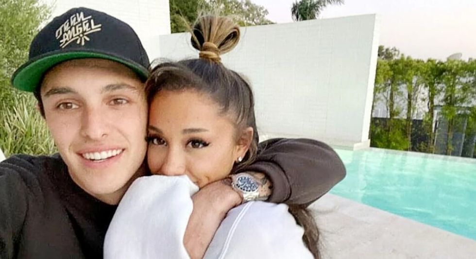 Ariana Grande in white sweater hugging husband Dalton Gomez who is wearing a black shirt and cap.