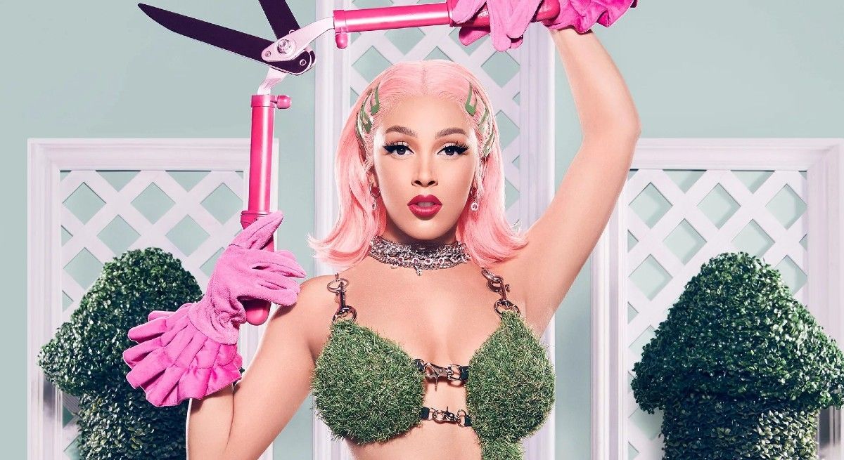 Doja Cat with pink hair and grass bra holding a pink lighter.