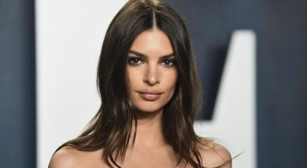 Model Emily Ratajkowski wearing her hair down and bare shoulders looks at the camera.