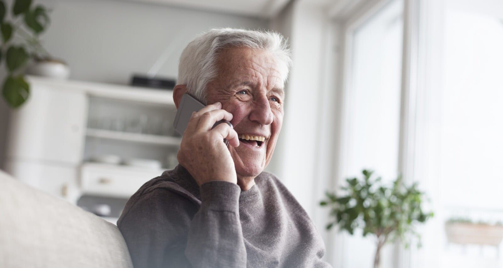 Portrait of laughing senior man telephoning with smartphone at home