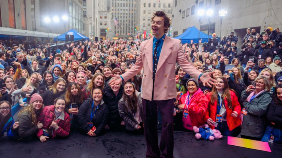 Harry Styles smiling in front of a crowd of fans in New York City.