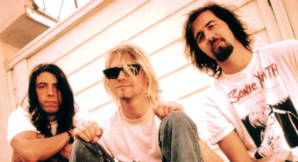 Kurt Cobain, Krist Novoselic, and Dave Grohl in white t-shirts sitting outside a house.