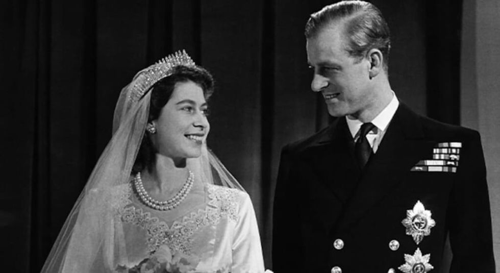 Black and white photo of a young Queen Elizabeth on her wedding day smiling at Prince Philip.