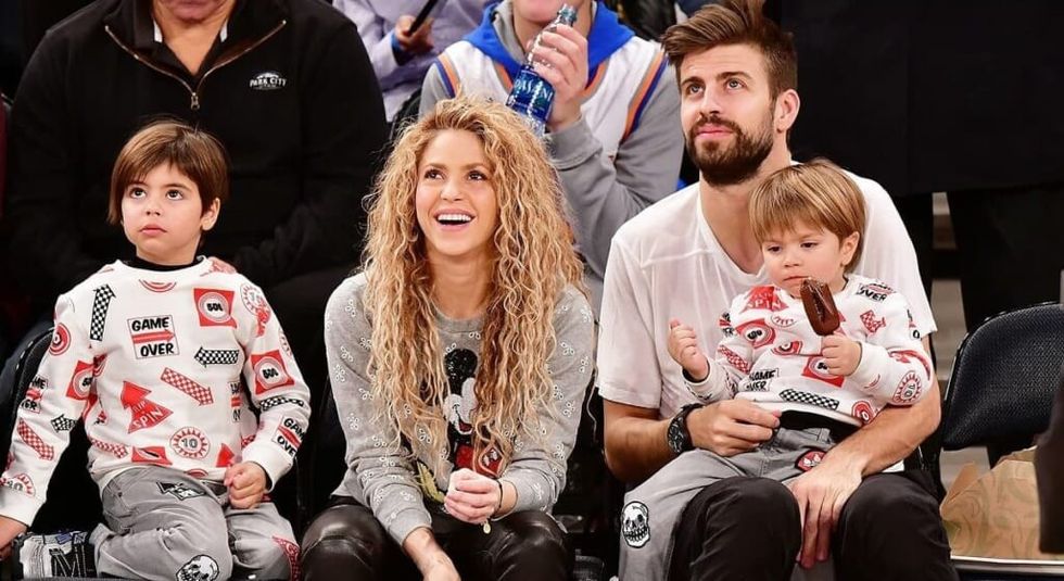 Shakira and husband and 2 children at a basketball game smiling and laughing.