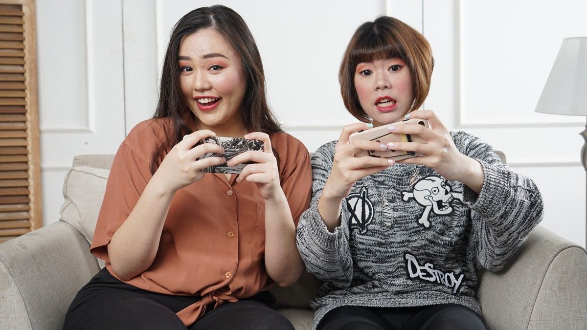 Two women play on their mobile phones on a couch