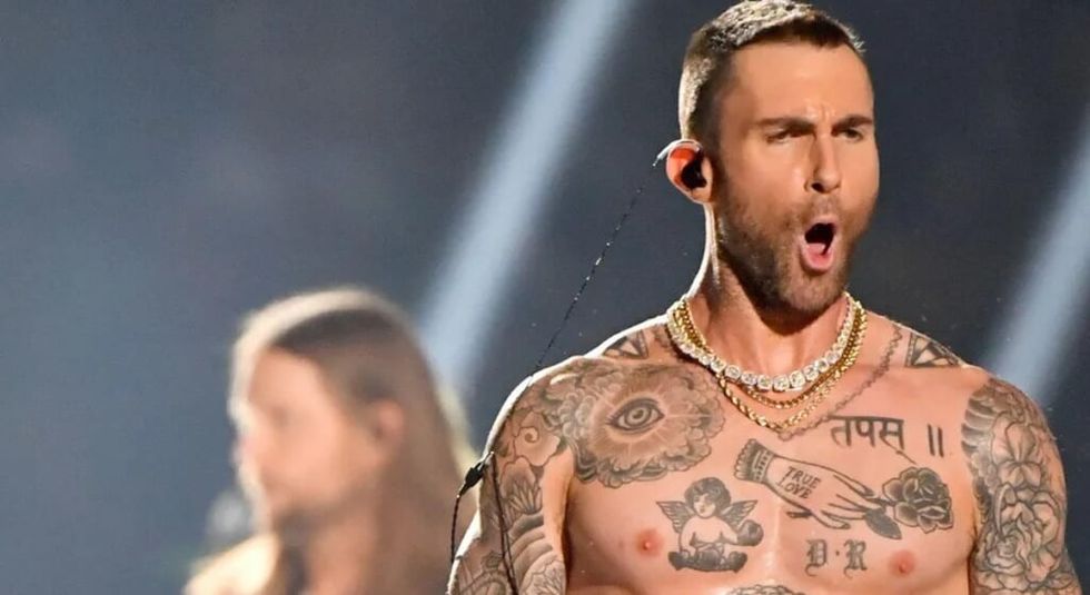 Adam Levine singing during a concert with bare chest showing off his tattoos.
