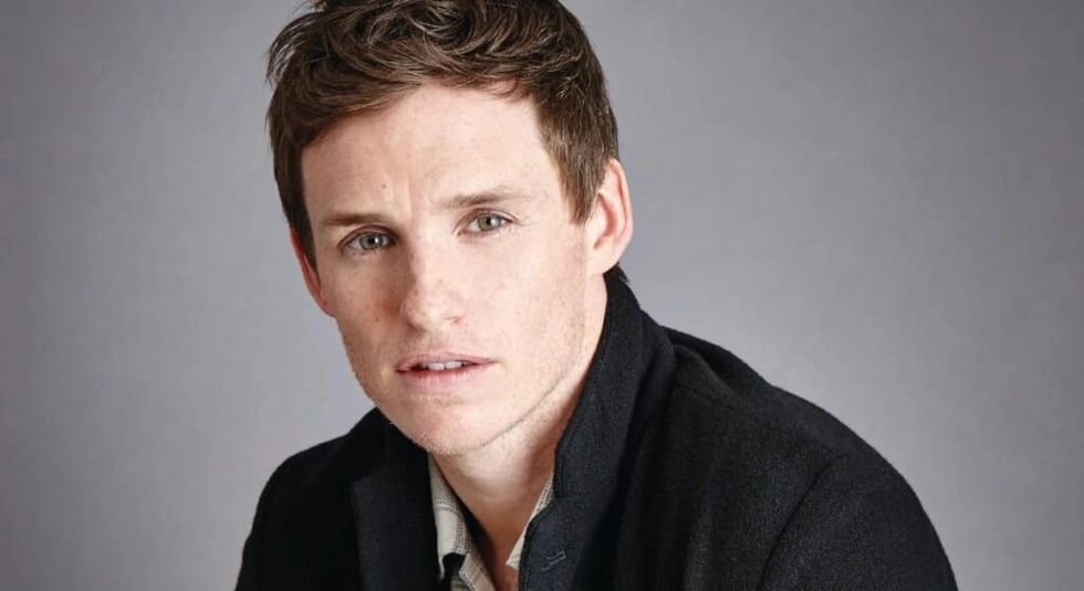Eddie Redmayne in black jacket and white shirt looking at the camera seriously.
