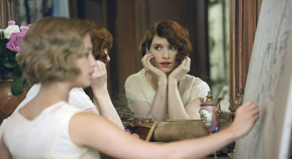 Eddie Redmayne in red wig and white blouse in The Danish Girl, looking in a mirror.