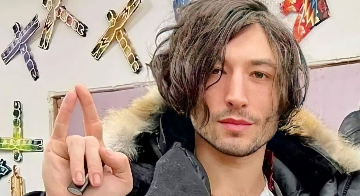 Ezra Miller in black winter jacket holding a lighter in his hand.