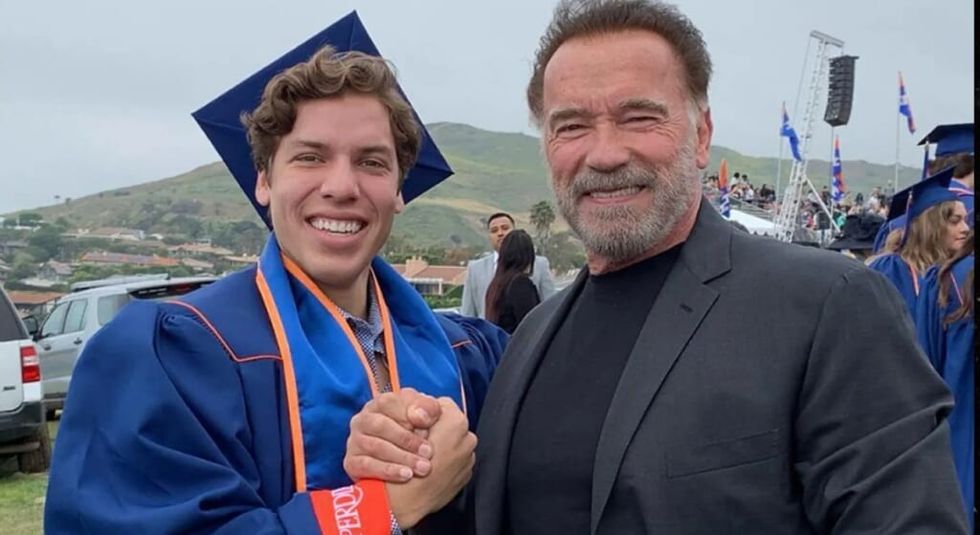 Joseph Baena wearing graduate cap and gown shaking his dad, Arnold  Schwarzenegger's hand.