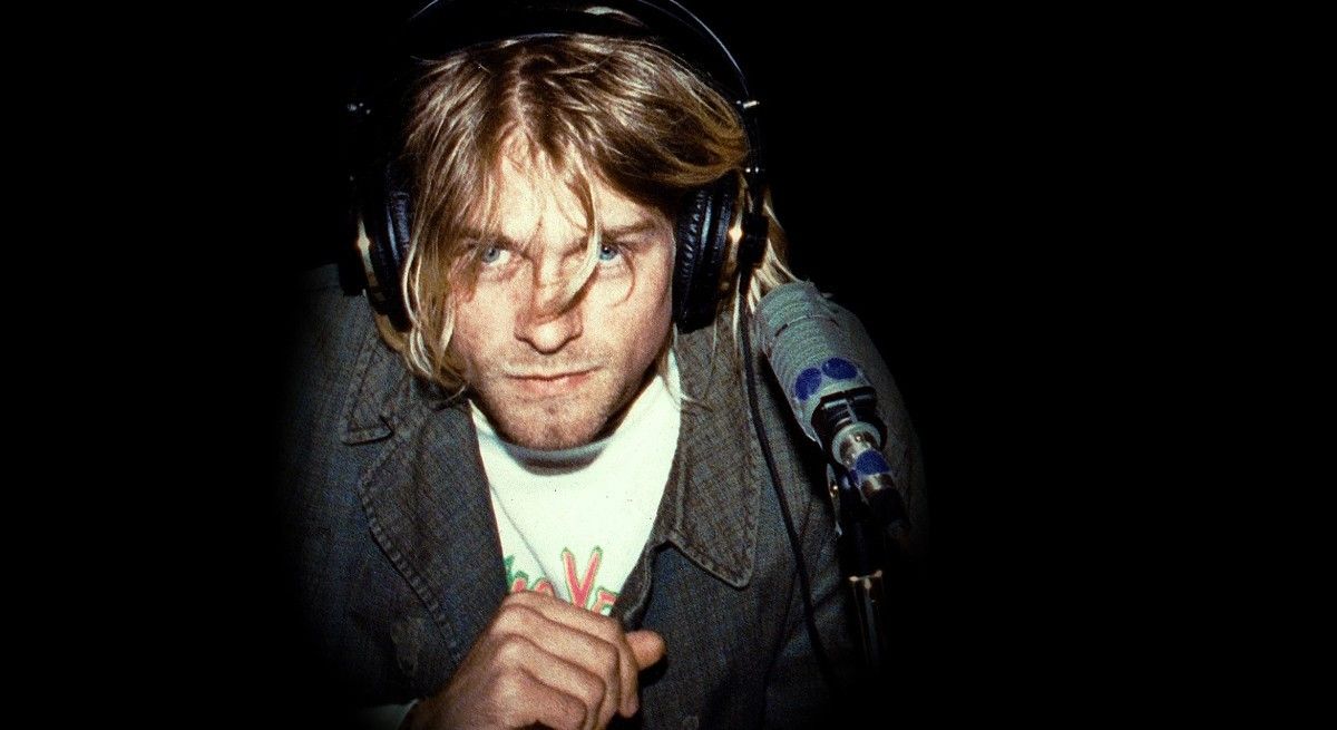 Kurt Cobain in cardigan leaning forward into the microphone.