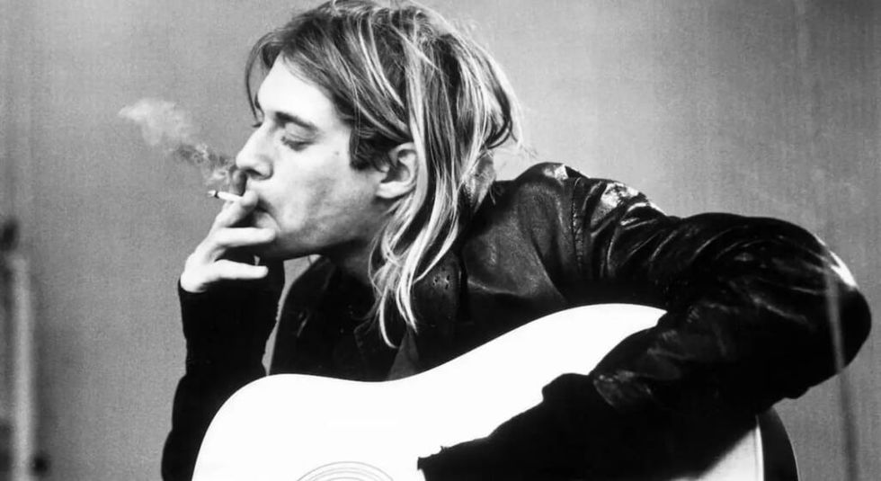 Black and white photo of Kurt Cobain playing the guitar and smoking.
