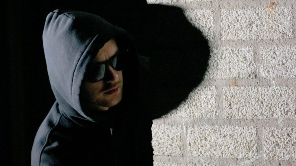 man in black hoodie and sunglasses near a wall