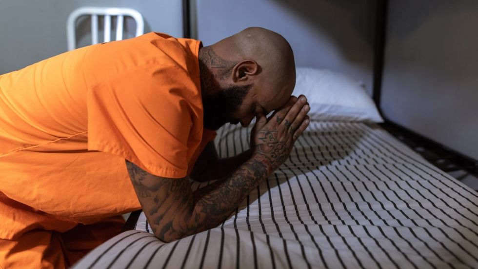 man in orange shirt praying on a bed