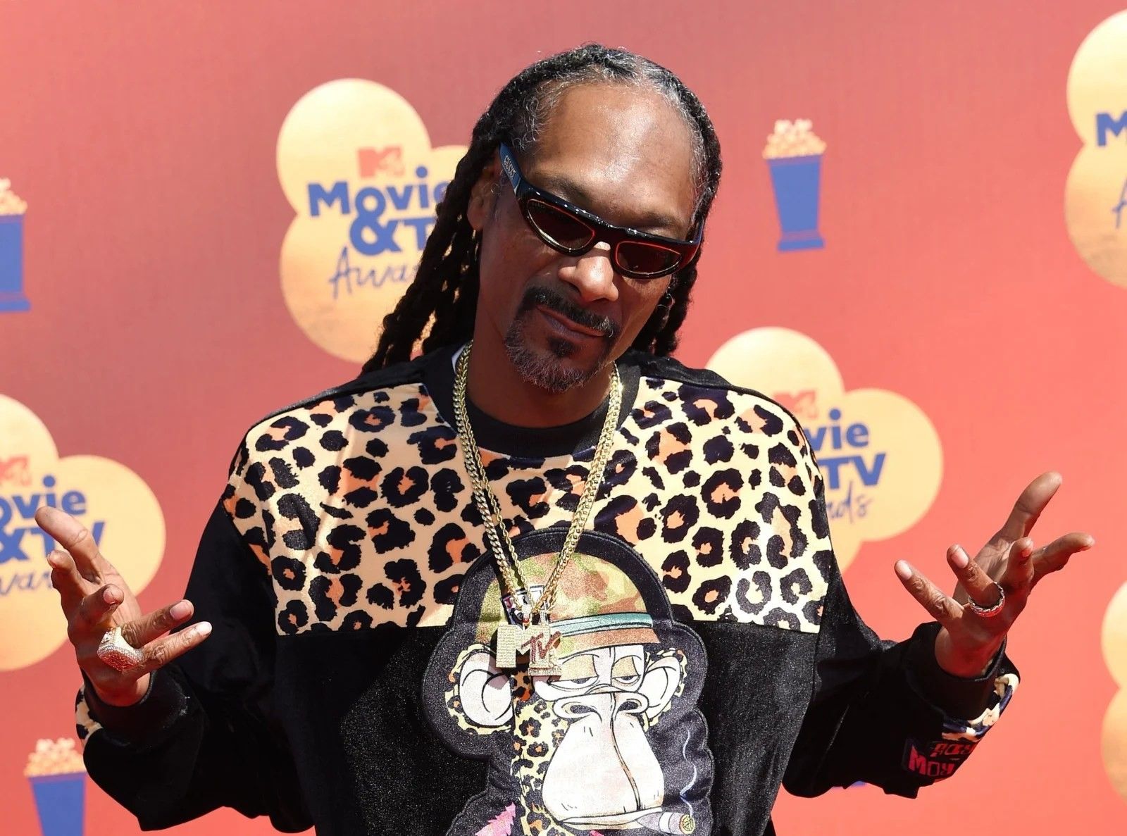 Snoop Dog wearing a leopard shirt with his hands in the air.