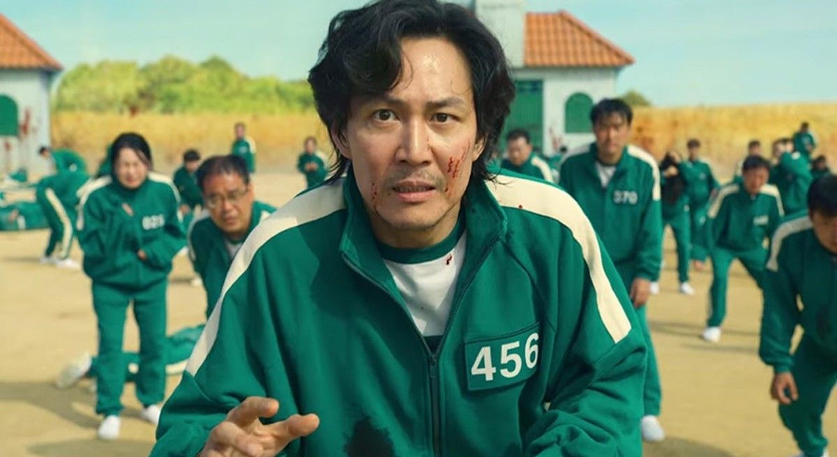 Squid Game's Lee Jung Jae in green track suit playing red light green light with blood on his face.