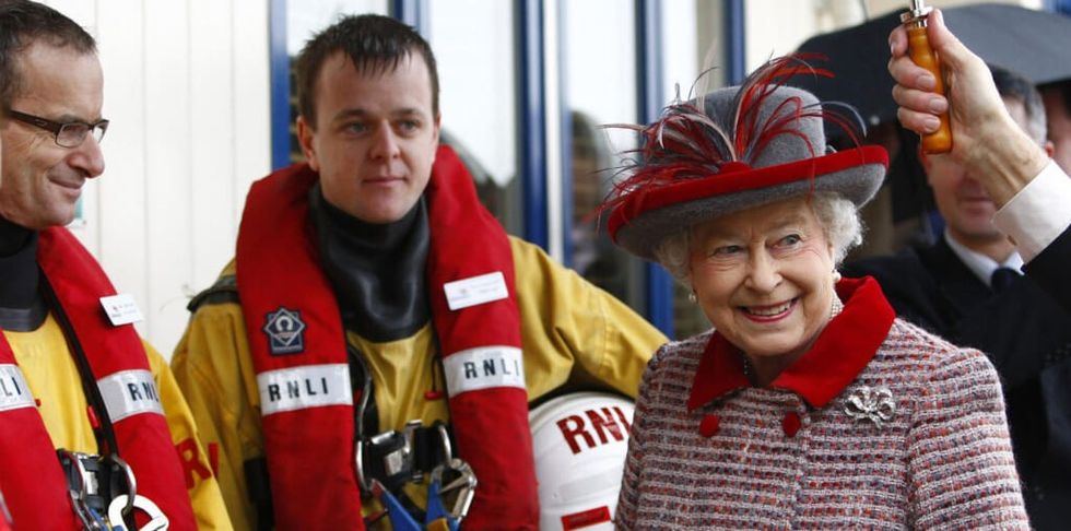 Queen Elizabeth with red and grey dress posing with firemen.