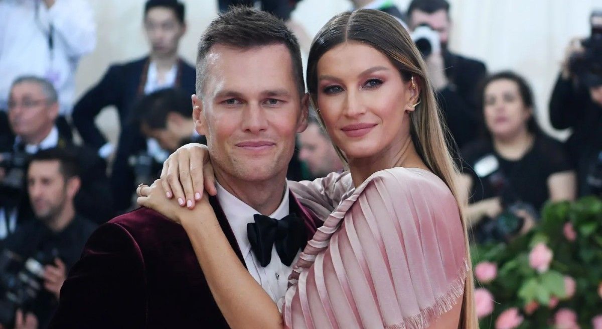 Tom Brady and wife Gisele Bundchen on the red carpet hugging and looking at the camera.