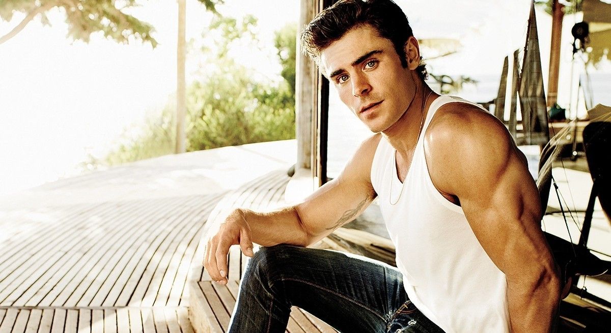 Zac Efron in white tank top showing off muscled arms.