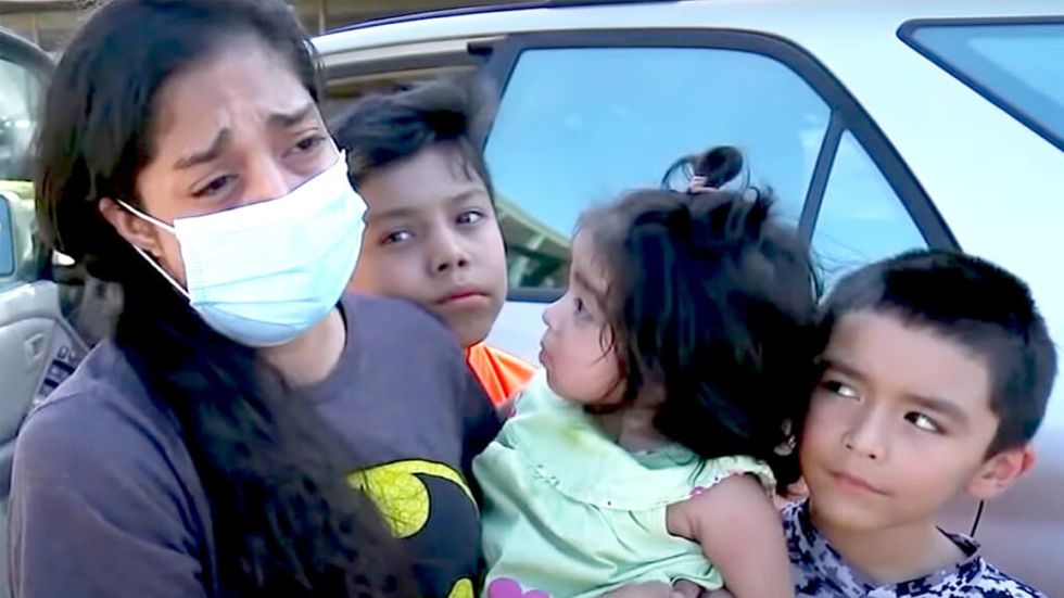 Young mother Kenia Madrigal wearing a covid mask and standing with 3 young children
