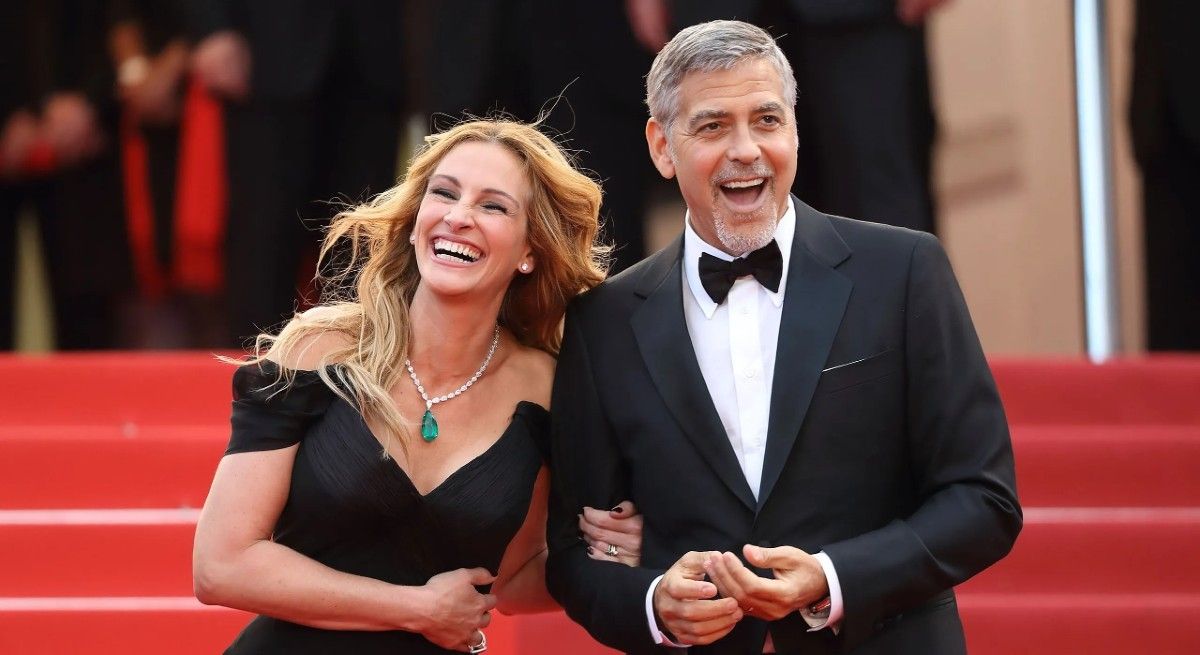 Julia Roberts and George Clooney in black tie laughing on the red carpet.