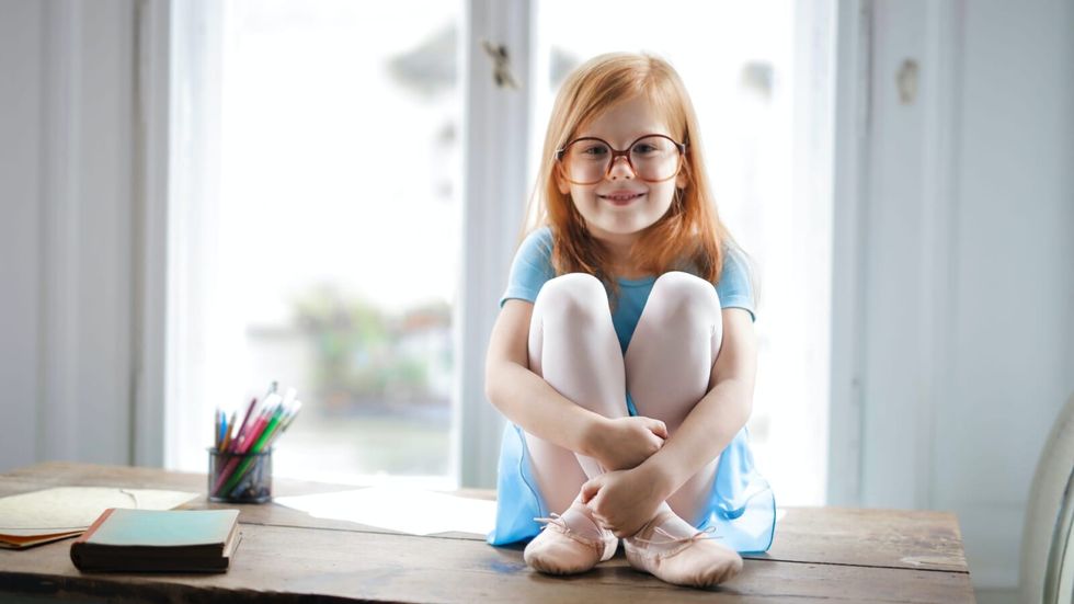 little girl in glasses sitting on a table